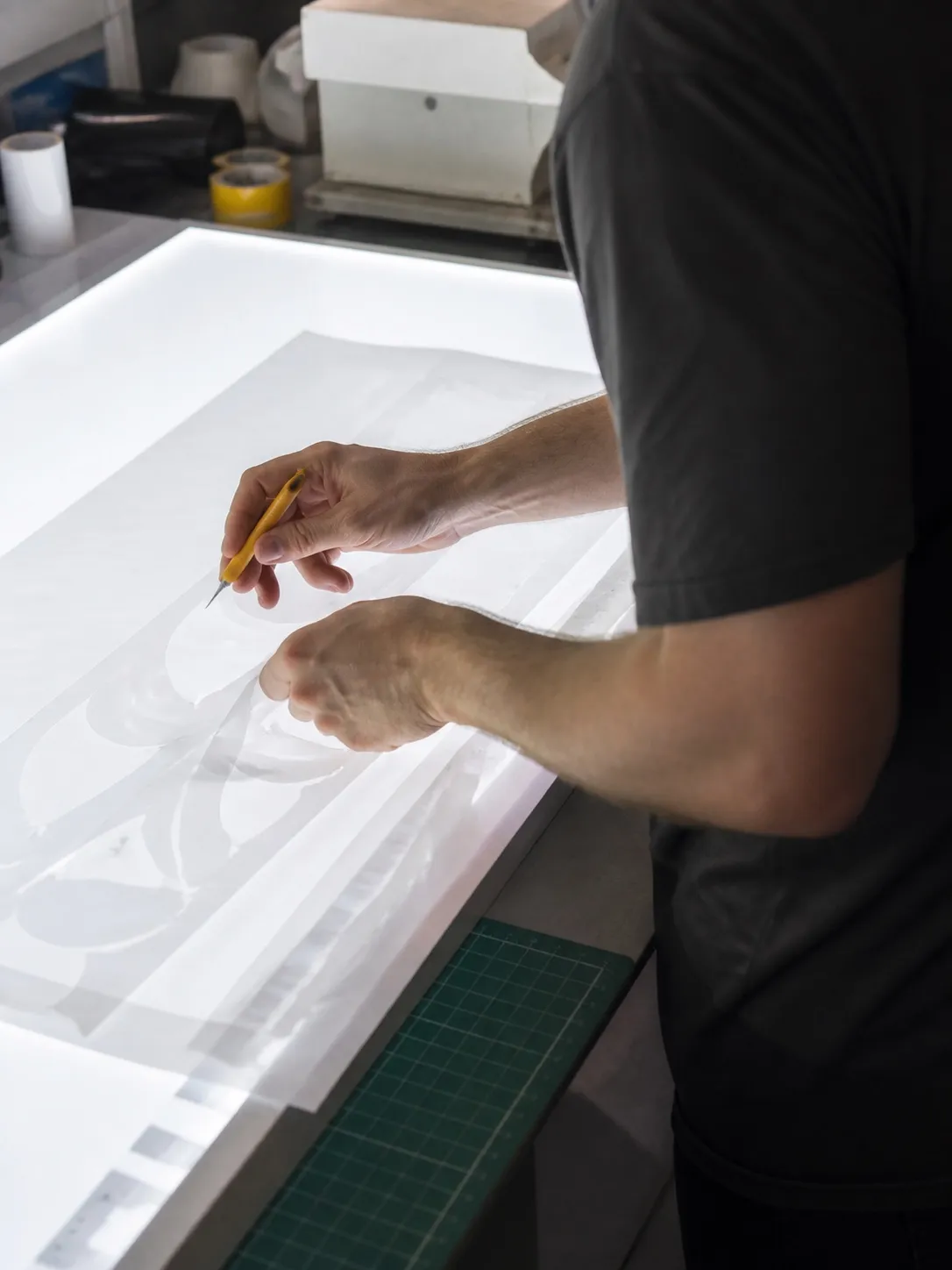 Worker seen from behind weeding blank vinyl shapes on a backlit fabrication bench