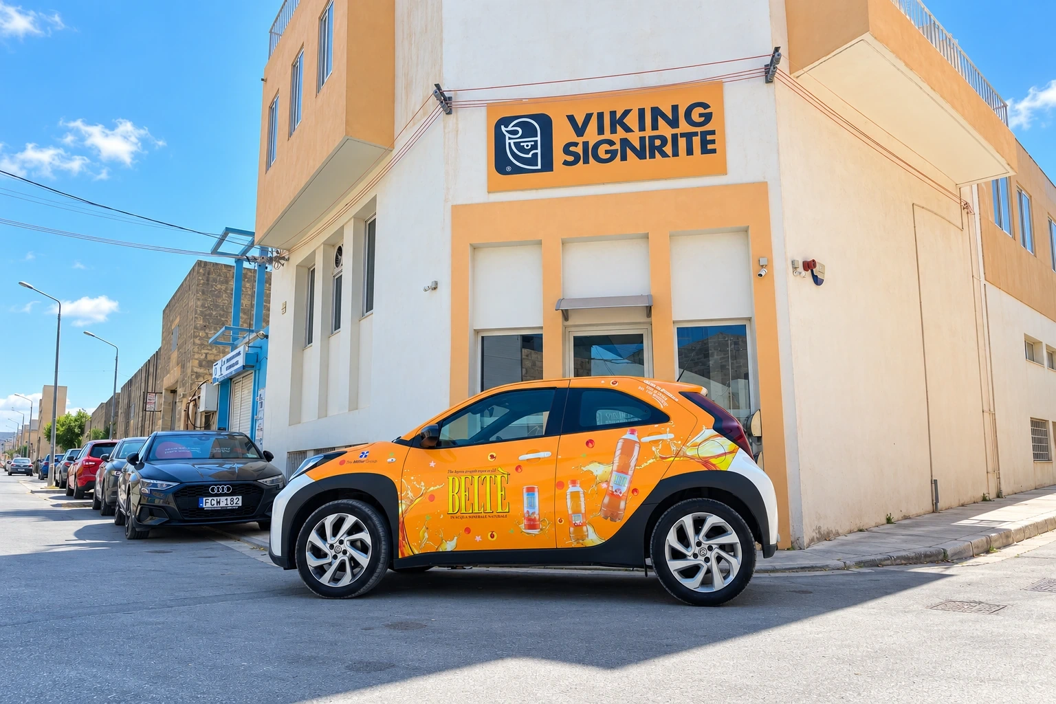 Compact car wrapped in an orange printed drinks design, parked in the sun outside the Viking Signrite workshop