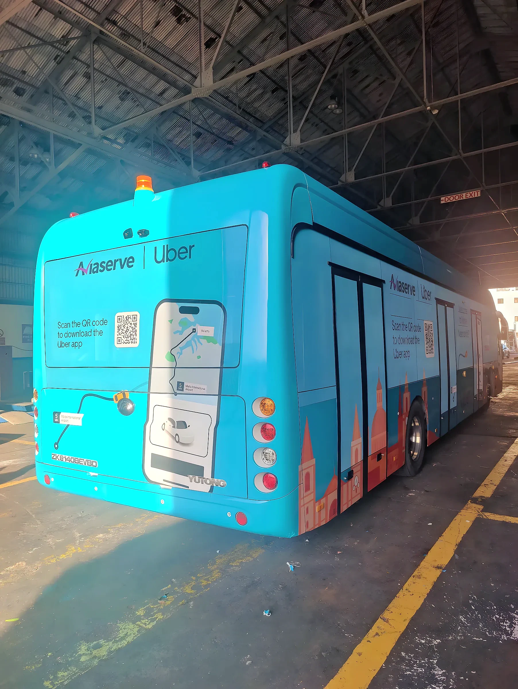 Turquoise wrapped bus with app download artwork on the rear and an illustrated skyline along its side