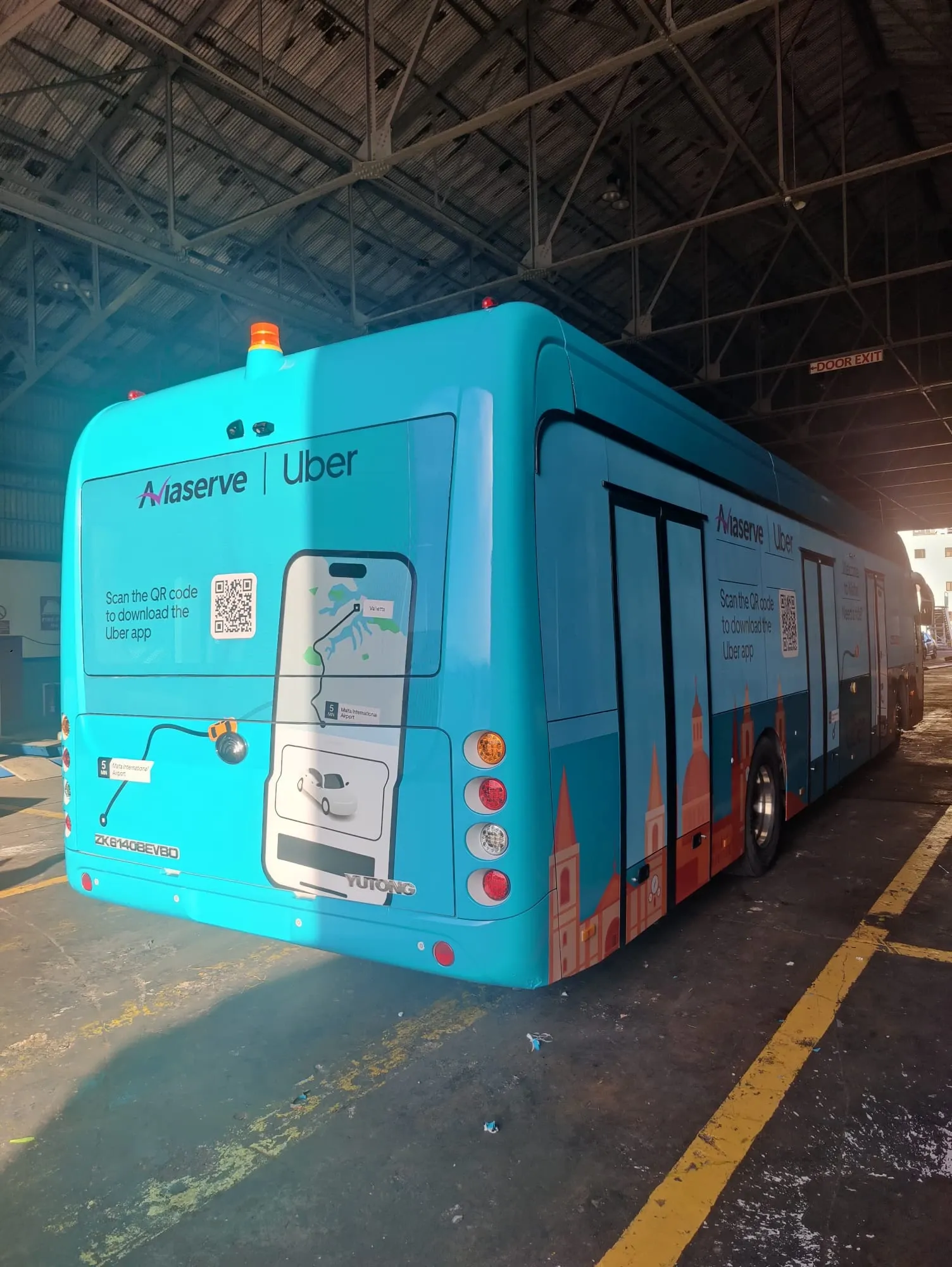 Turquoise wrapped bus with app download artwork on the rear and an illustrated skyline along its side