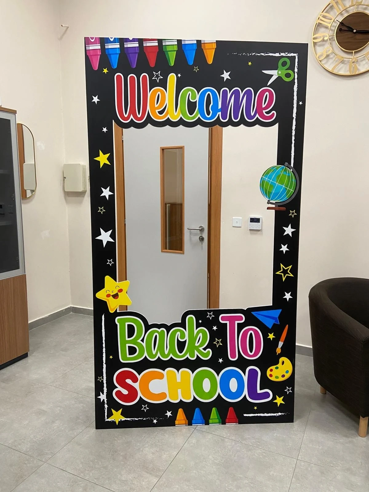 Tall free-standing cut-out photo frame printed with colourful Welcome and Back to School lettering, standing in an office