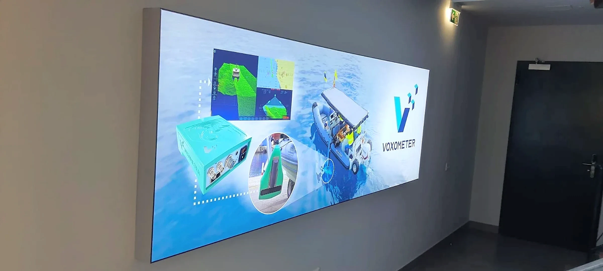 Wide backlit wall panel printed with marine survey equipment photography in a dark corridor