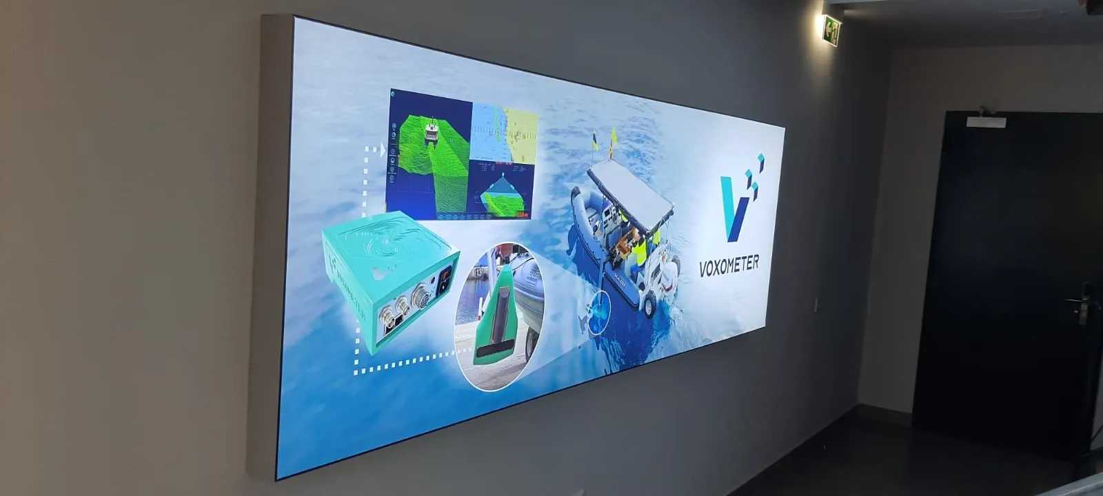 Wide backlit wall panel printed with marine survey equipment photography in a dark corridor
