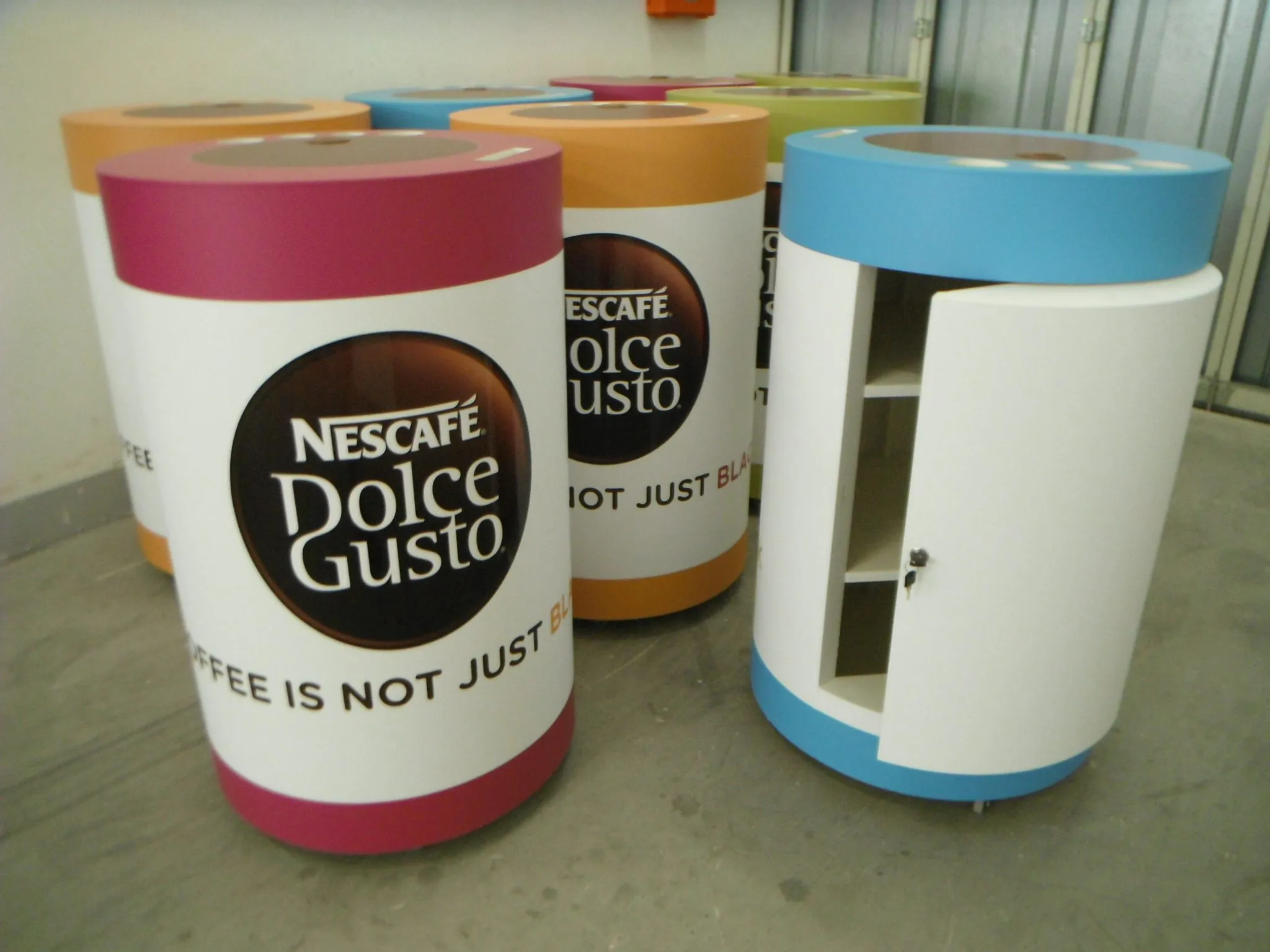 Two cylindrical display units printed as oversized coffee cups, one with an open storage door