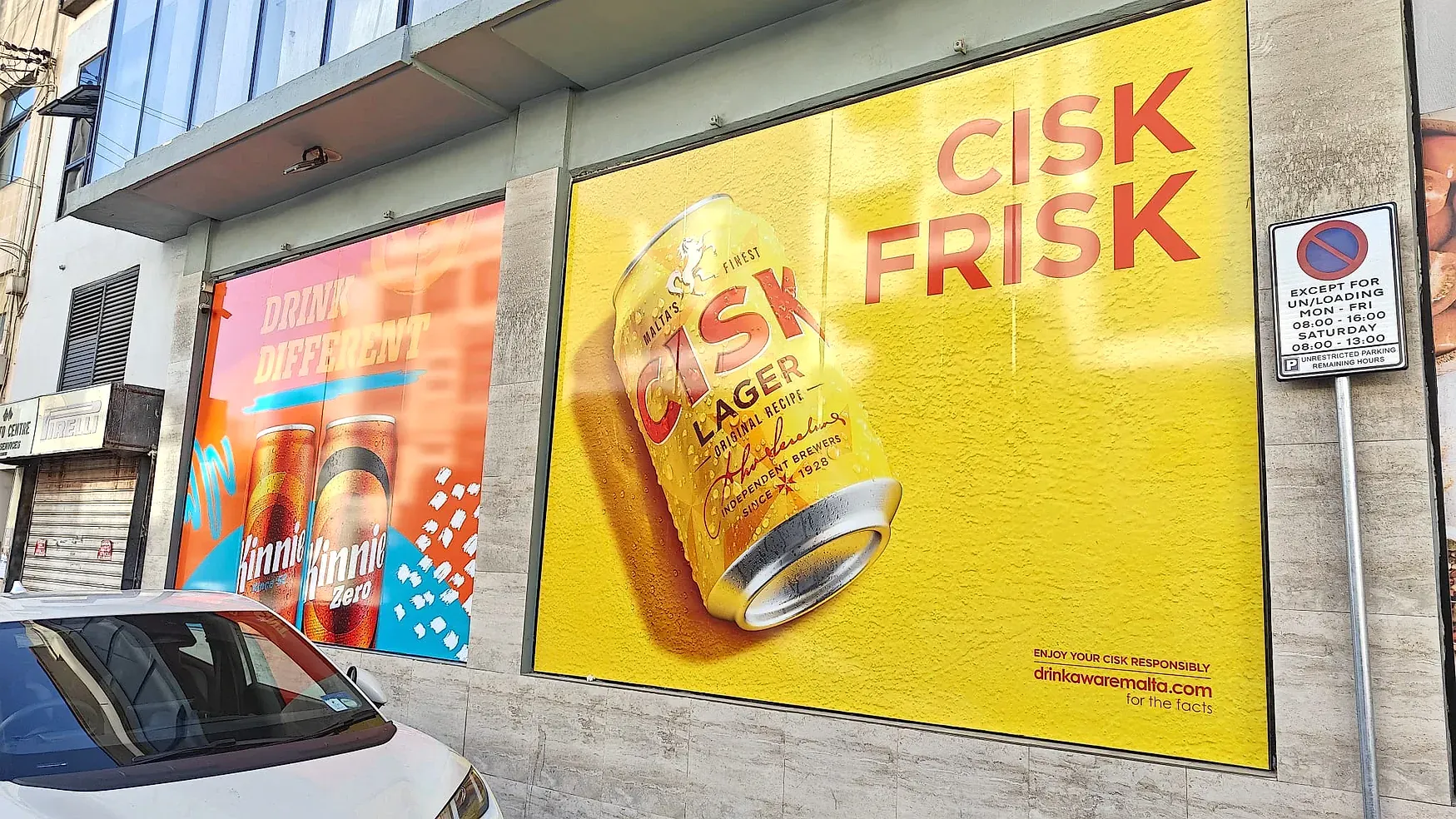 Yellow window graphic of a lager can beside a pink panel of soft drink cans on a street frontage