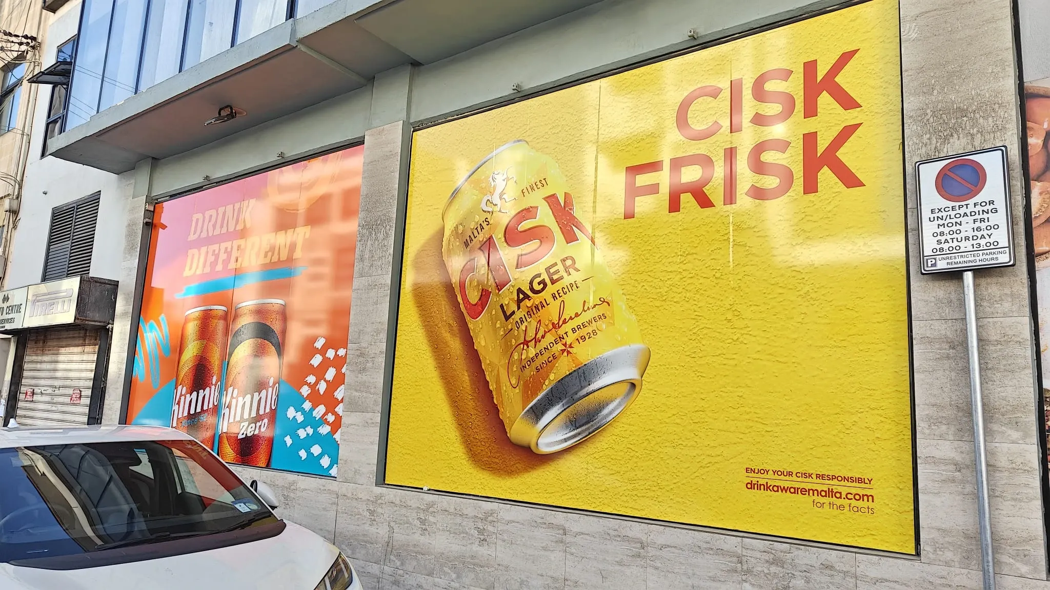 Yellow window graphic of a lager can beside a pink panel of soft drink cans on a street frontage