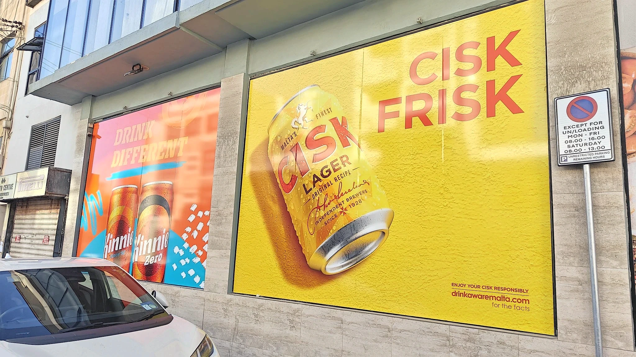 Yellow window graphic of a lager can beside a pink panel of soft drink cans on a street frontage