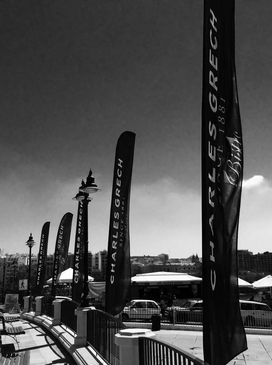 Row of dark feather flags along a promenade railing, photographed in black and white