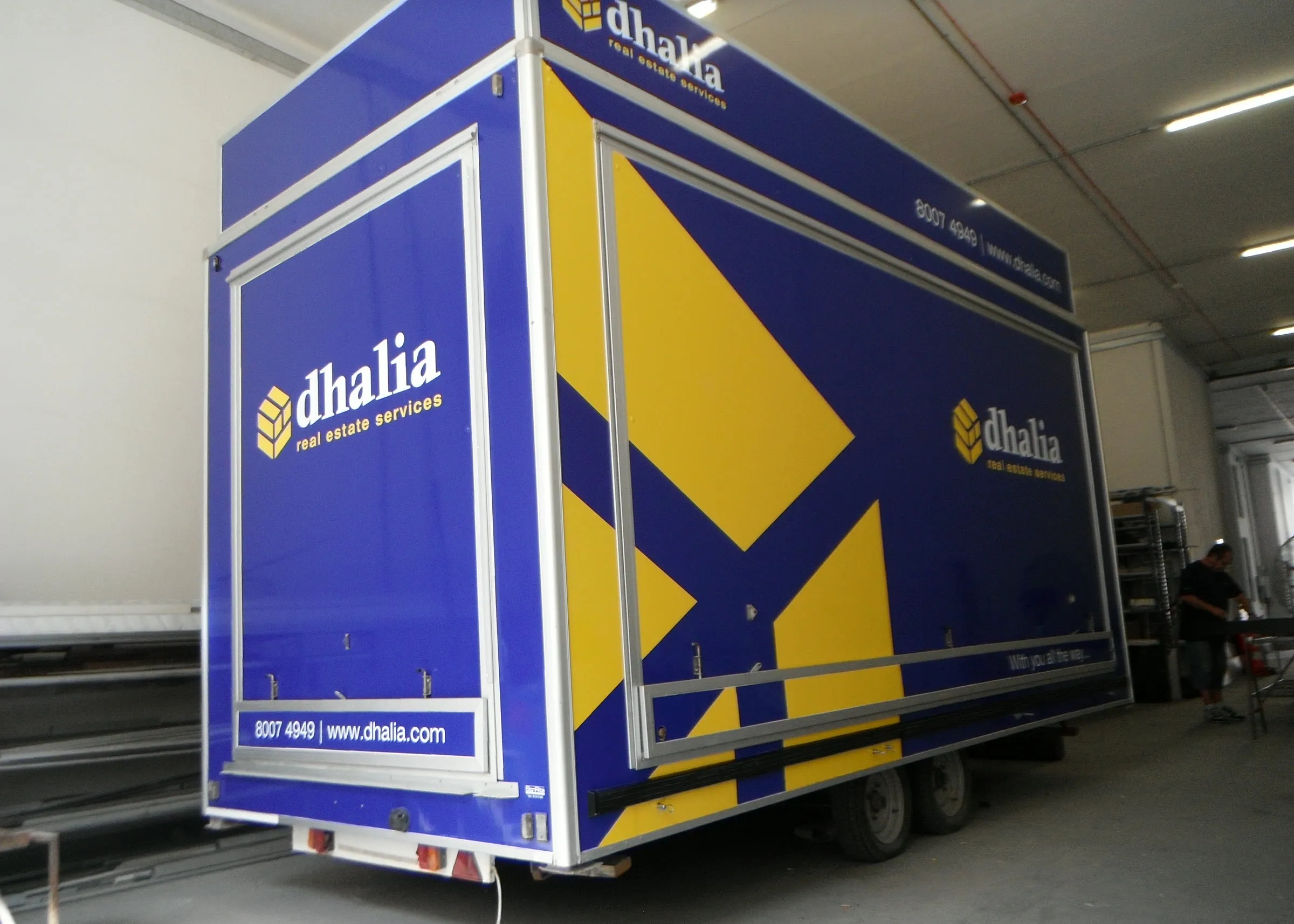 Deep blue box lorry with yellow geometric graphics viewed from the rear three-quarter angle