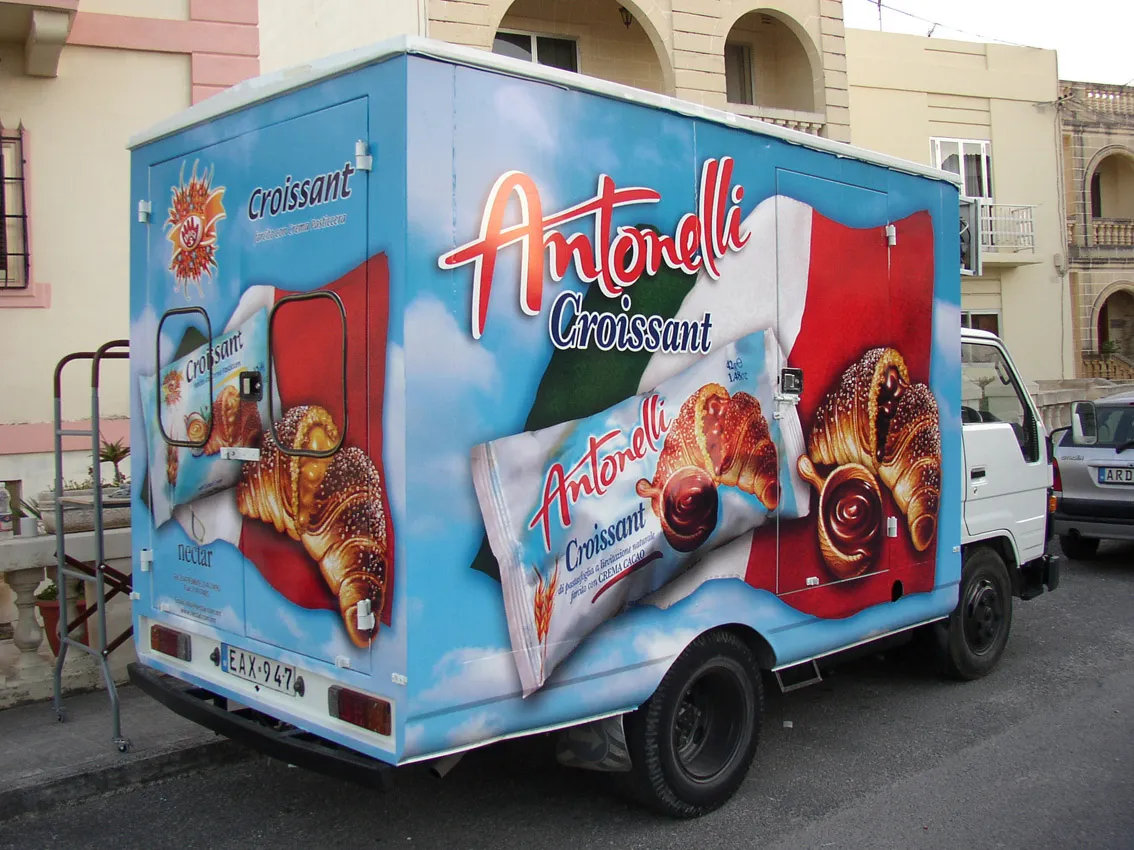 Box truck wrapped in a sky ground with product pack photography and a flag motif, the print continuing across the rear door hinges and around the corner