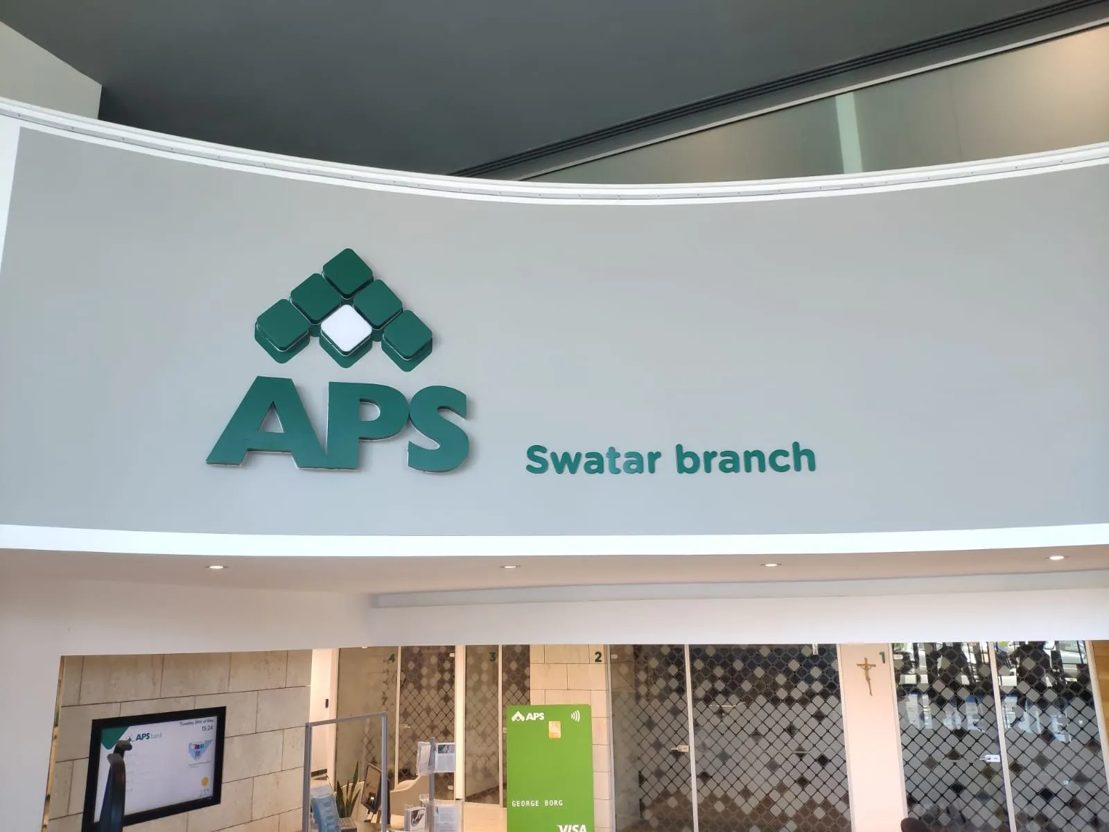 Green cut-out logo and branch name mounted on a white curved interior wall