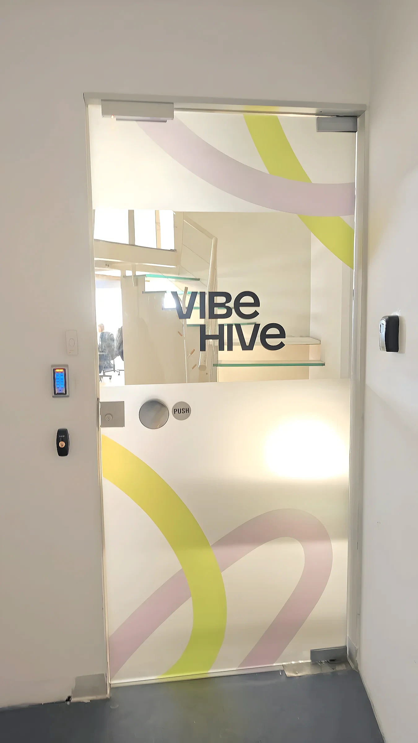 Glass door with frosted film printed in yellow and pink curves, the company name readable through a clear band