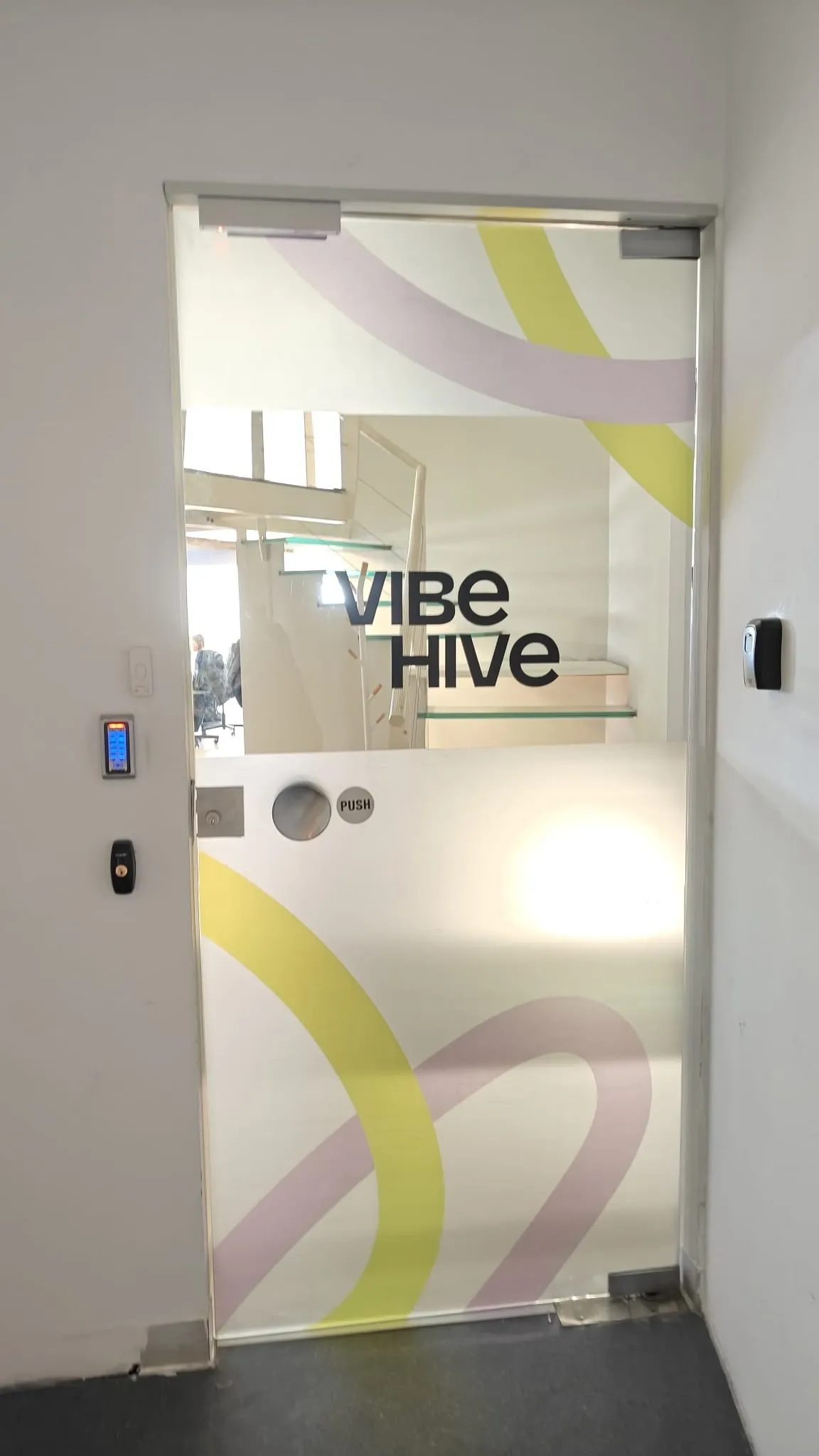 Glass door with frosted film printed in yellow and pink curves, the company name readable through a clear band