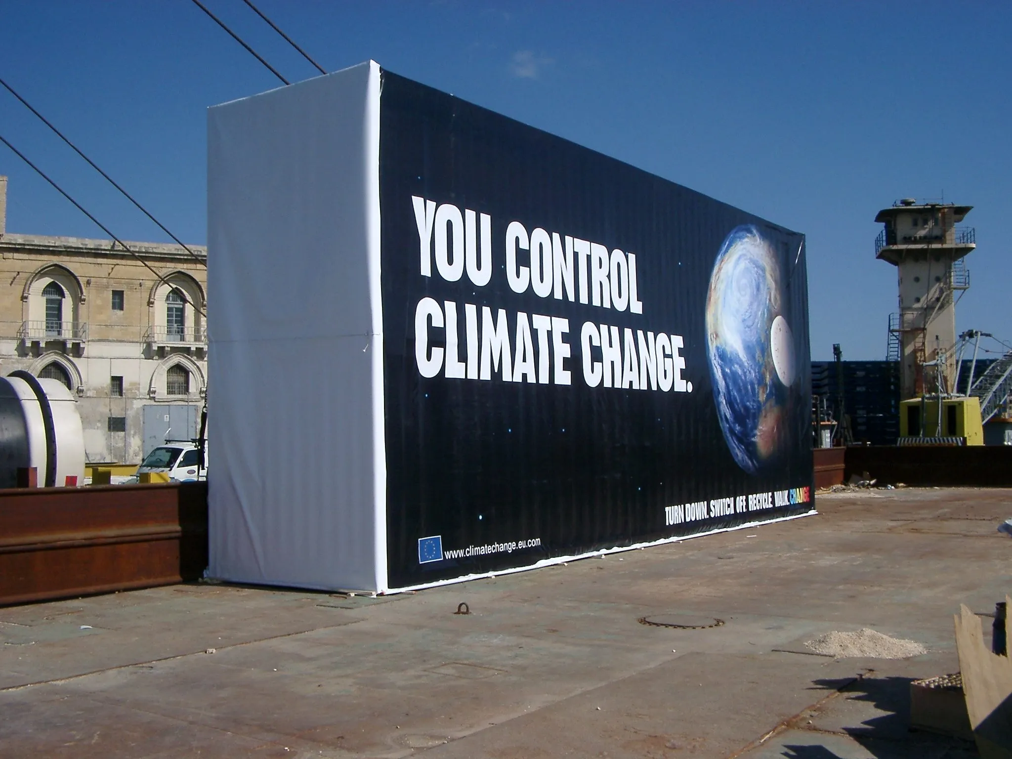 Large dark banner printed with a campaign line and a globe, covering a site hoarding