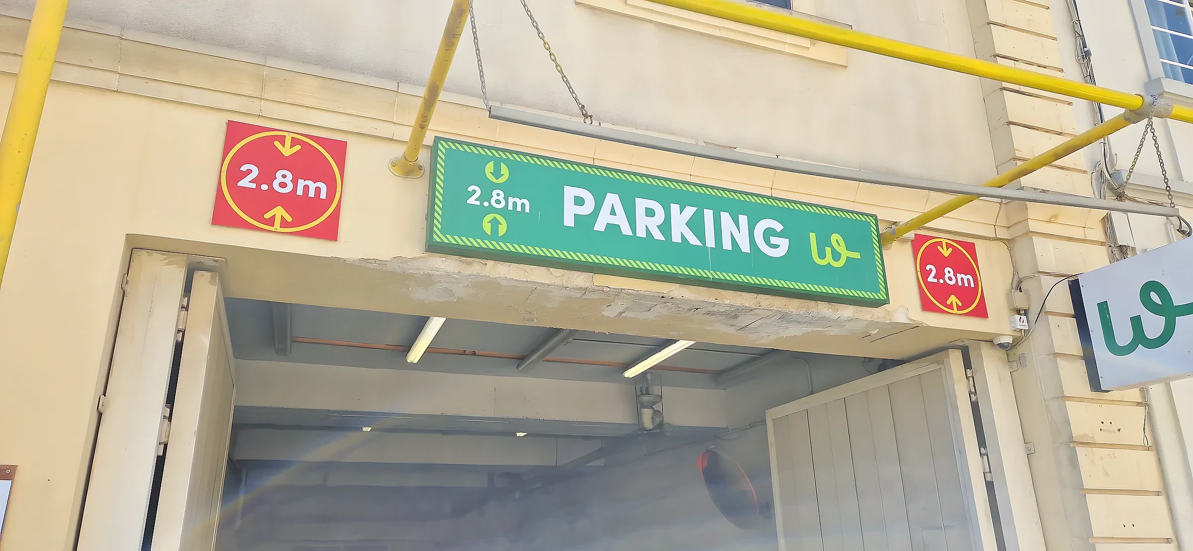 Green parking sign showing a 2.8 metre height limit between two red height warning plates over a car park entrance