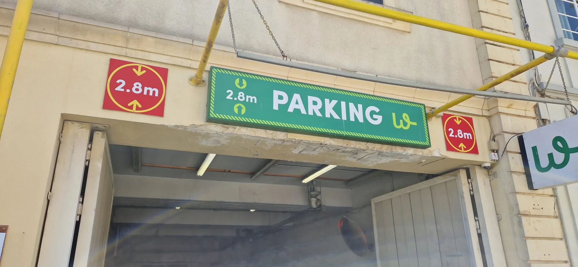 Green parking sign showing a 2.8 metre height limit between two red height warning plates over a car park entrance