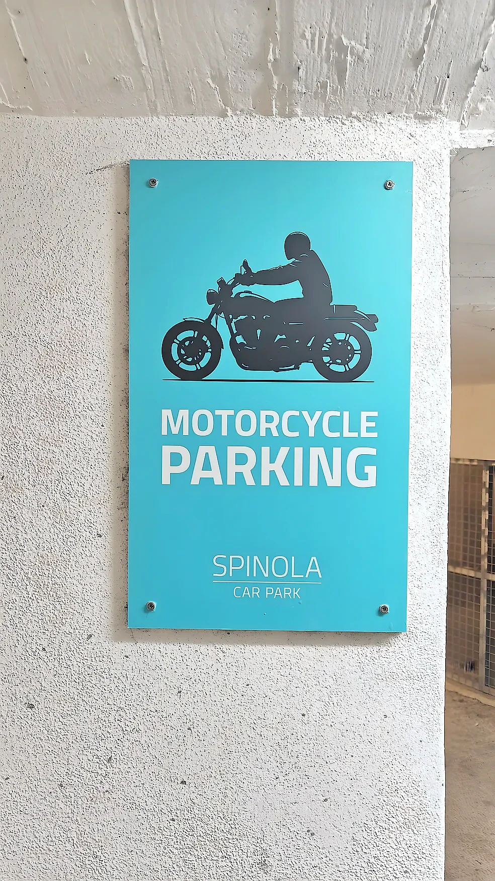 Turquoise motorcycle parking sign screw-fixed to a white concrete car park wall
