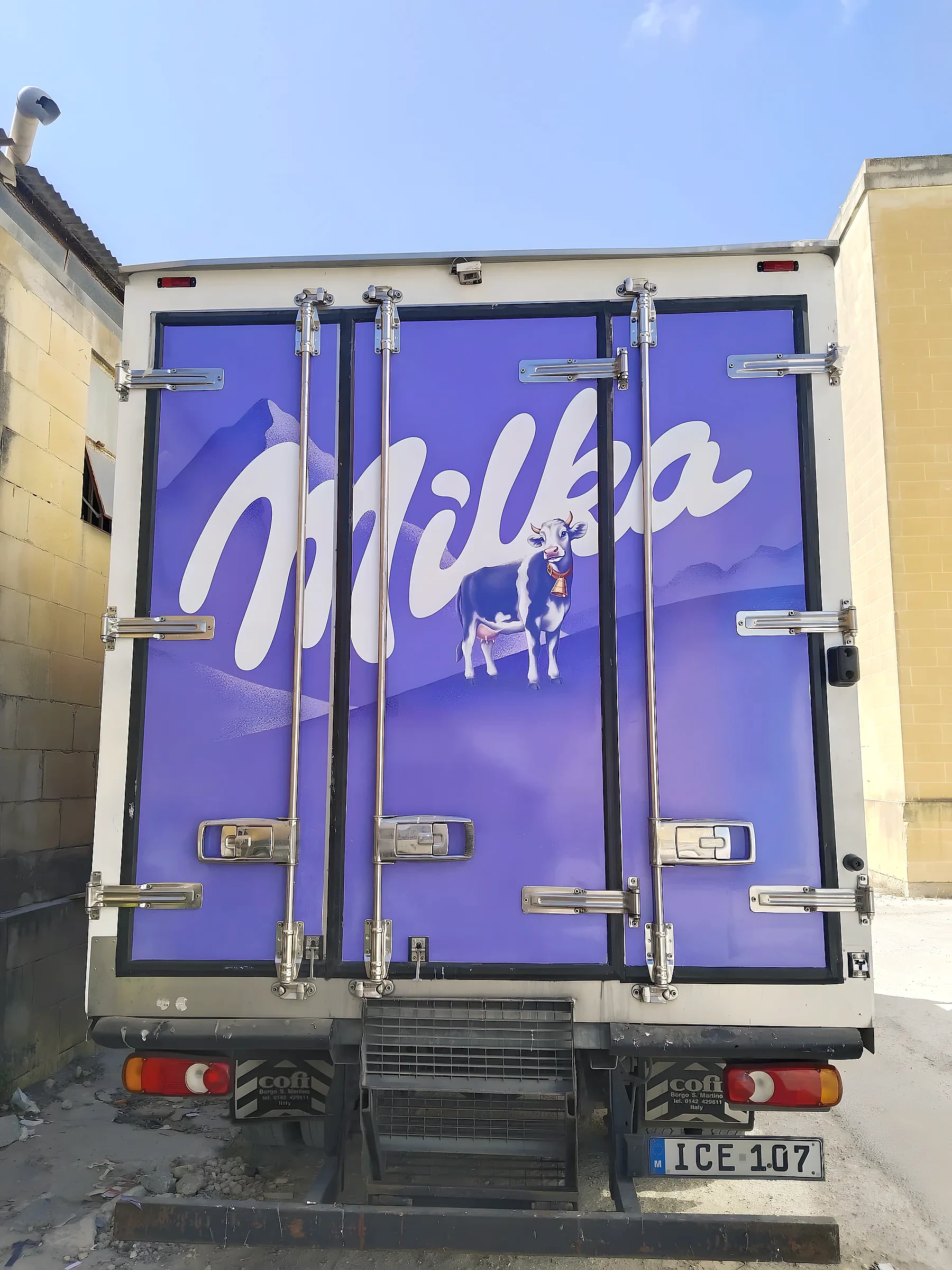 Purple wrapped rear doors of a refrigerated truck with a brand name and a cow illustration