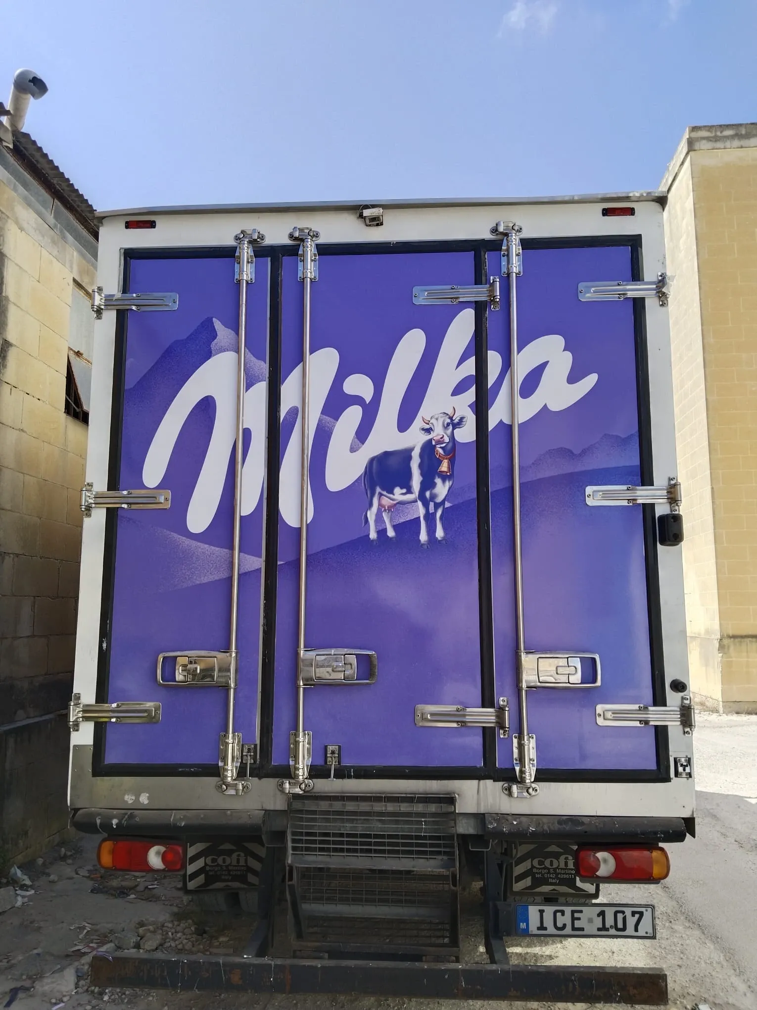 Purple wrapped rear doors of a refrigerated truck with a brand name and a cow illustration