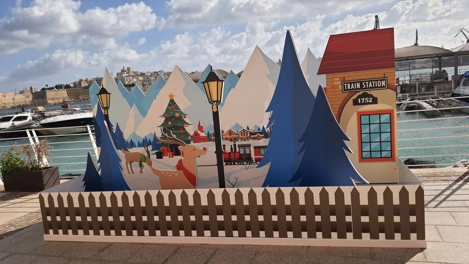 Layered cut-out Christmas village scene with mountains, trees and a station house on a waterfront promenade