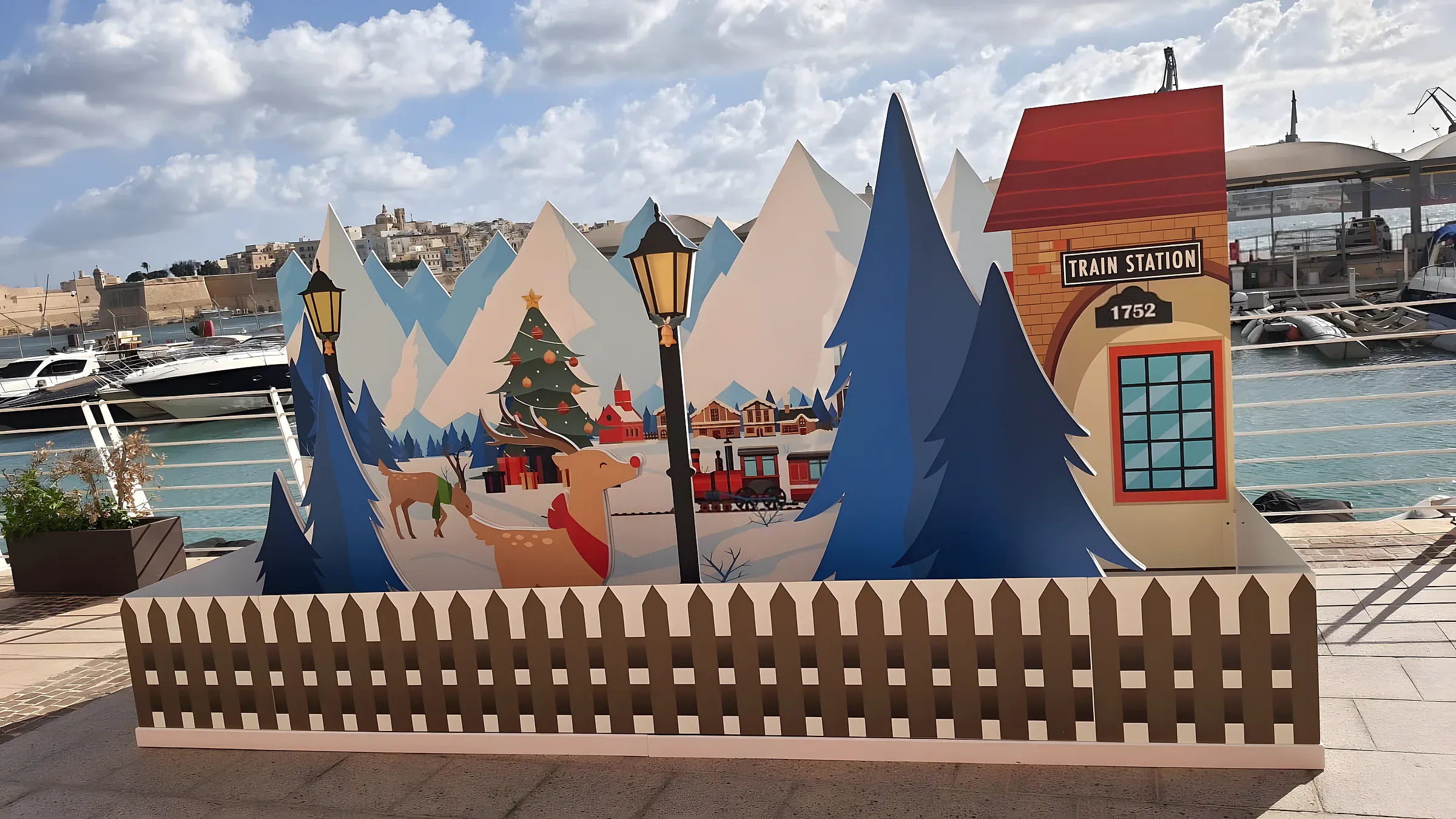 Layered cut-out Christmas village scene with mountains, trees and a station house on a waterfront promenade
