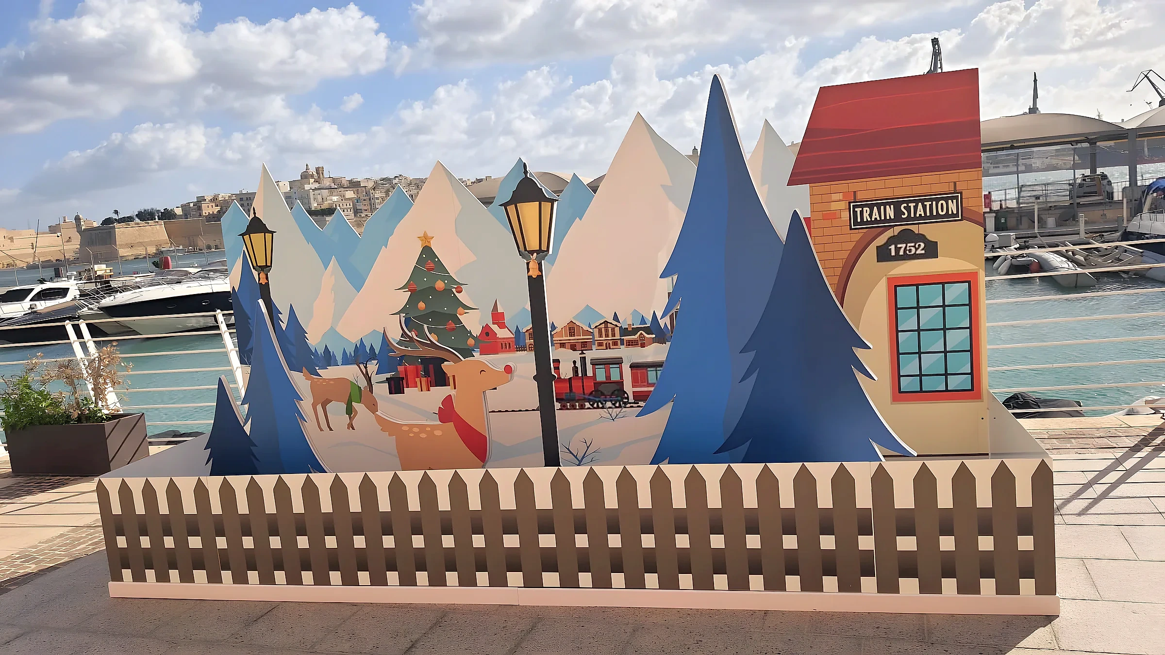 Layered cut-out Christmas village scene with mountains, trees and a station house on a waterfront promenade