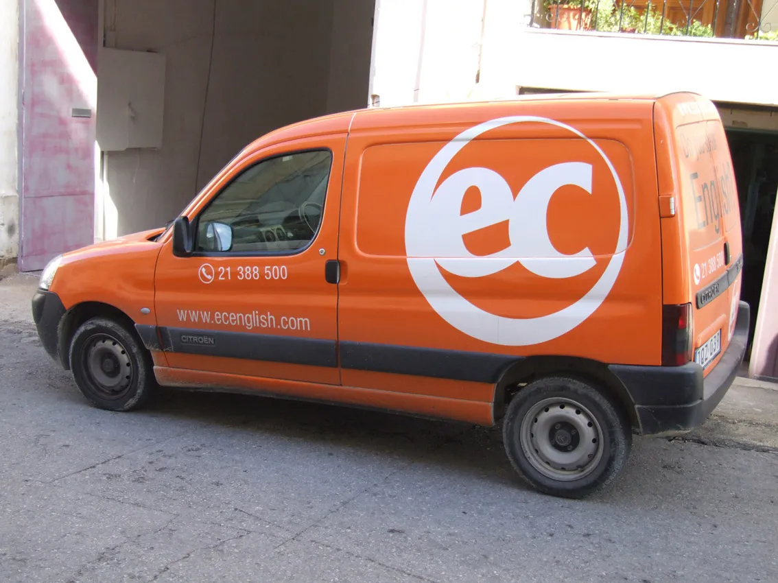 Small van in a full orange colour-change wrap with a very large white roundel mark on the flank, phone number and web address on the front door