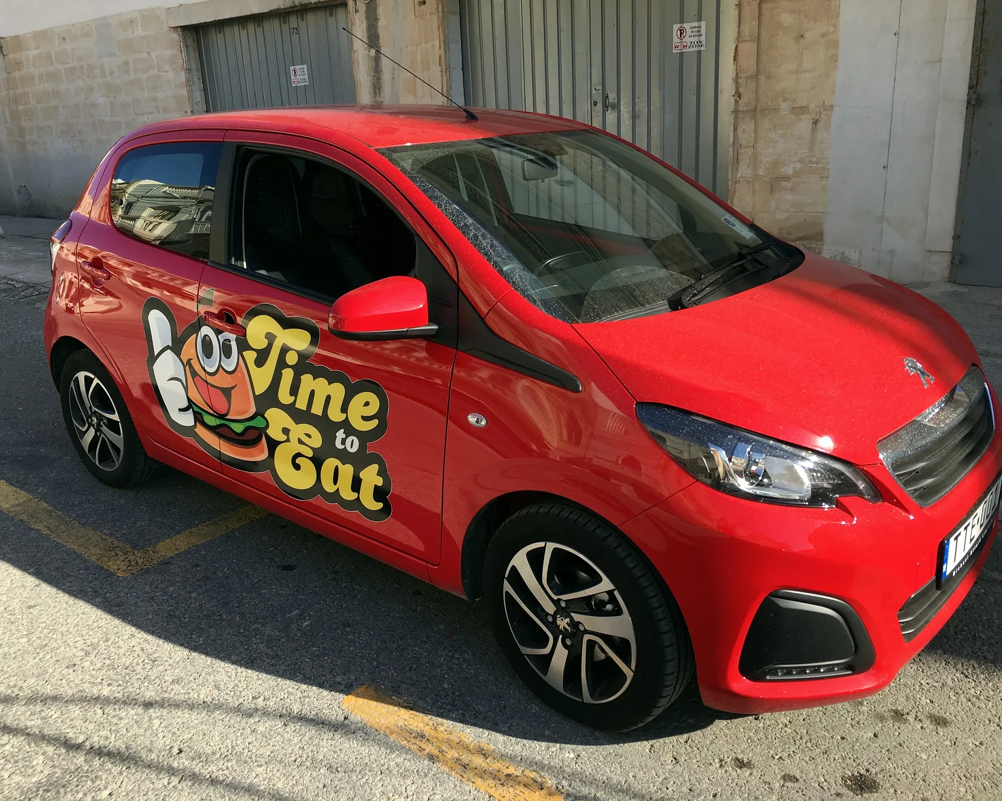 Red compact city car with bold illustrated side graphics viewed from the front three-quarter angle