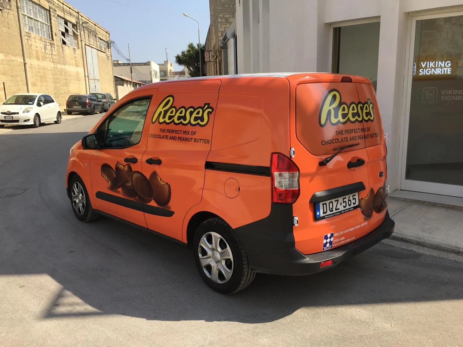 Orange compact van wrapped with a confectionery graphic, viewed from the rear three-quarter angle