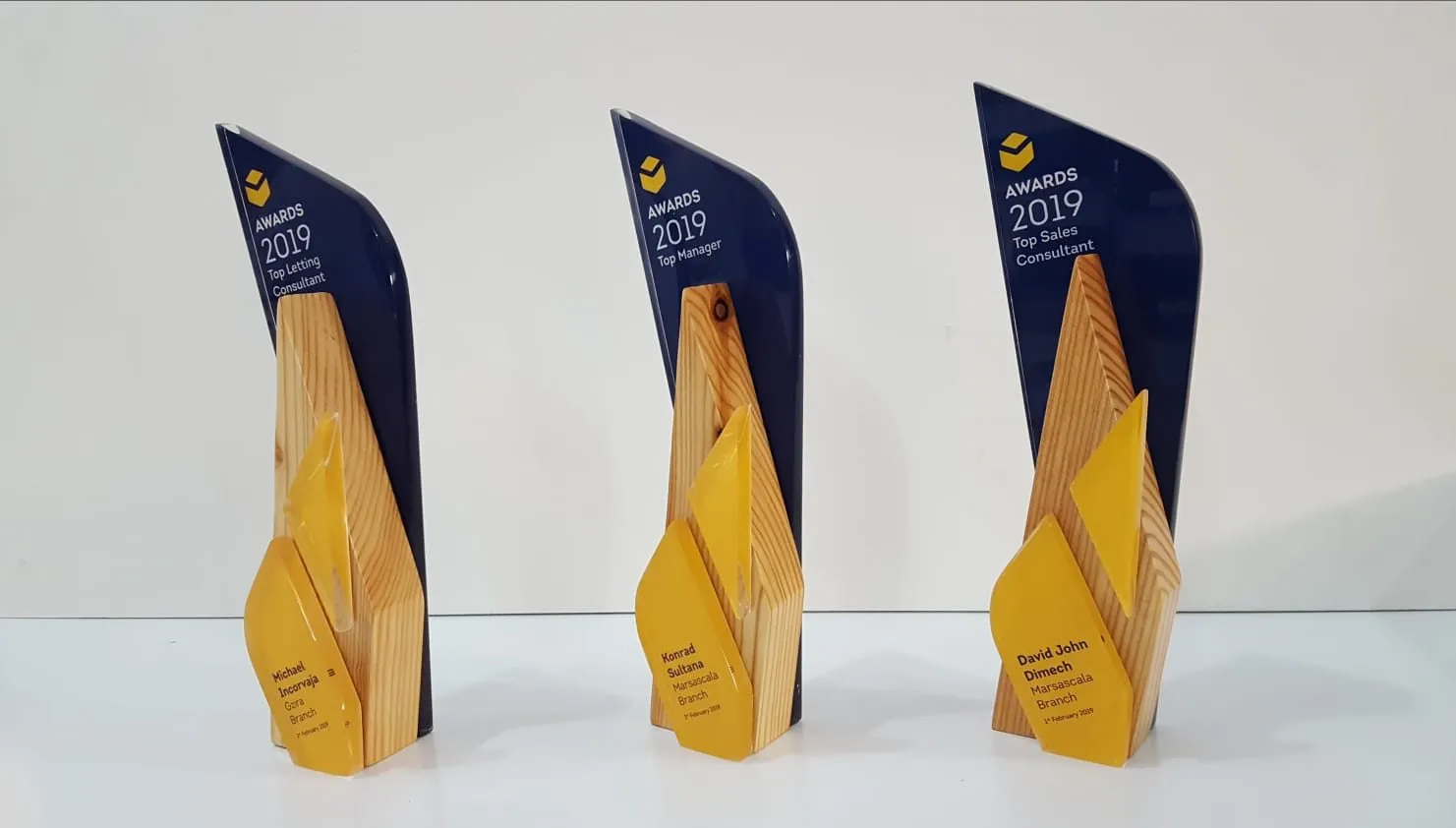 Three angular awards with timber bases and dark blue printed acrylic blades on a white surface