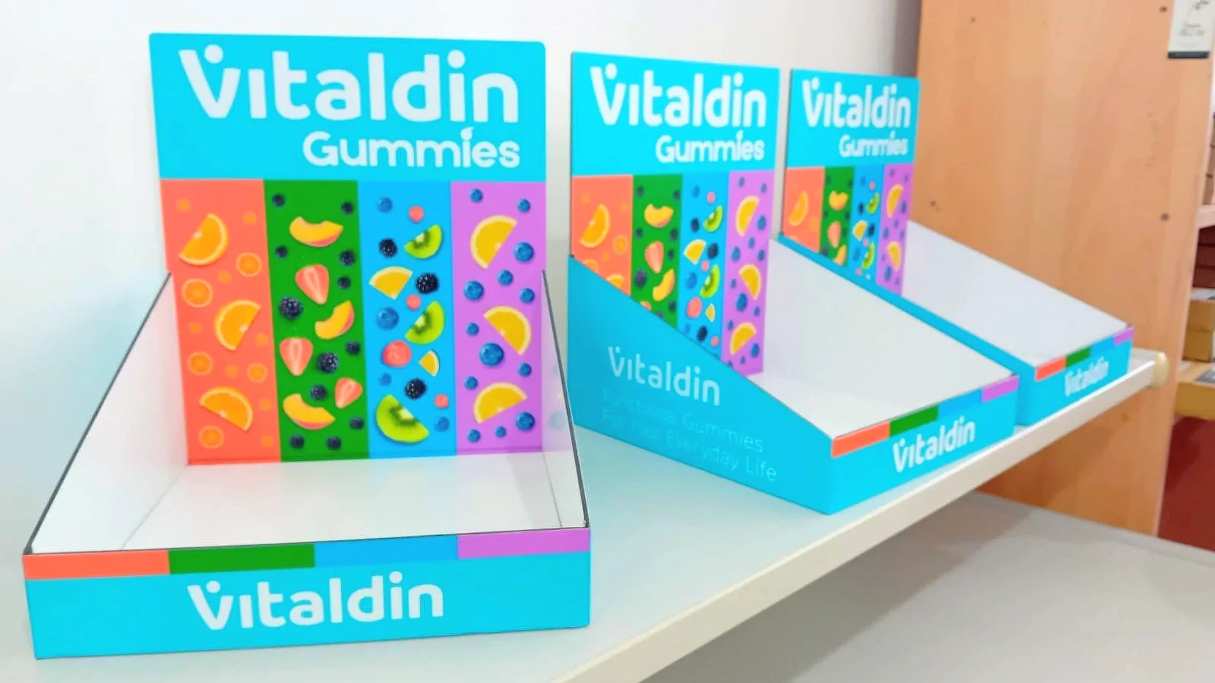 Three turquoise printed counter display trays for vitamin gummies on a white shelf