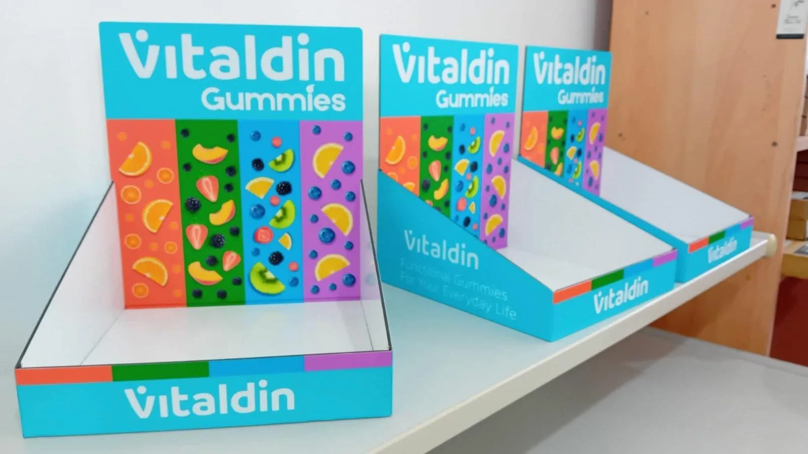 Three turquoise printed counter display trays for vitamin gummies on a white shelf