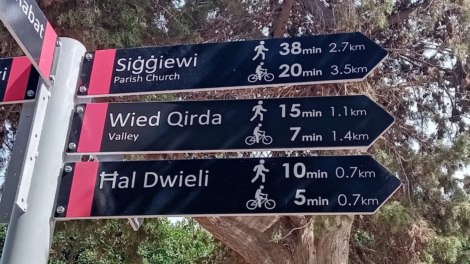 Three black fingerpost arms giving walking and cycling times to Maltese villages and a valley