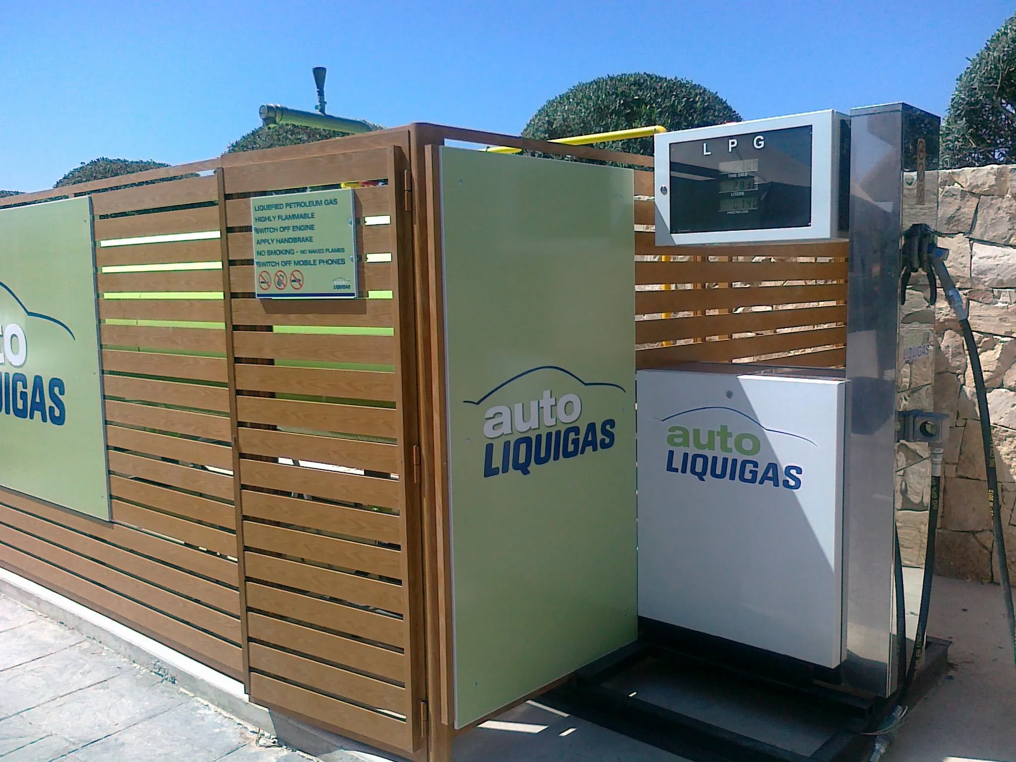 Timber-slatted enclosure with a green branded panel installed against a wall at a forecourt
