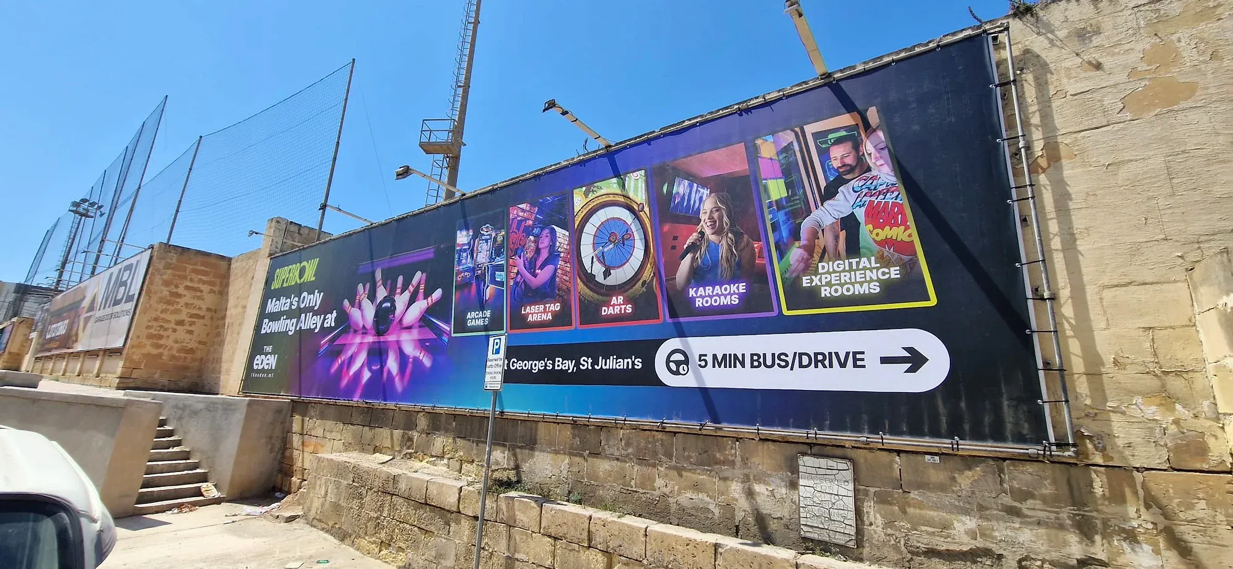 Wide dark banner with photographic panels for bowling, darts and karaoke rooms fixed along a stone site hoarding