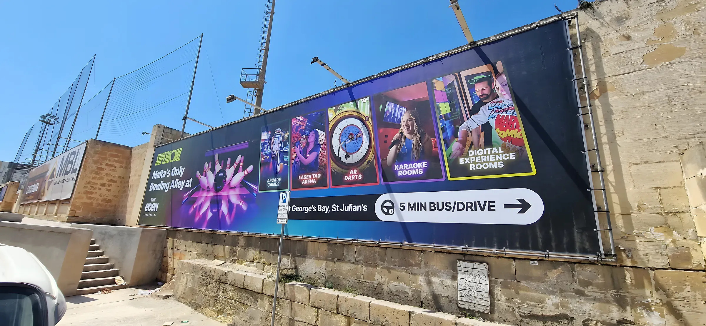 Wide dark banner with photographic panels for bowling, darts and karaoke rooms fixed along a stone site hoarding