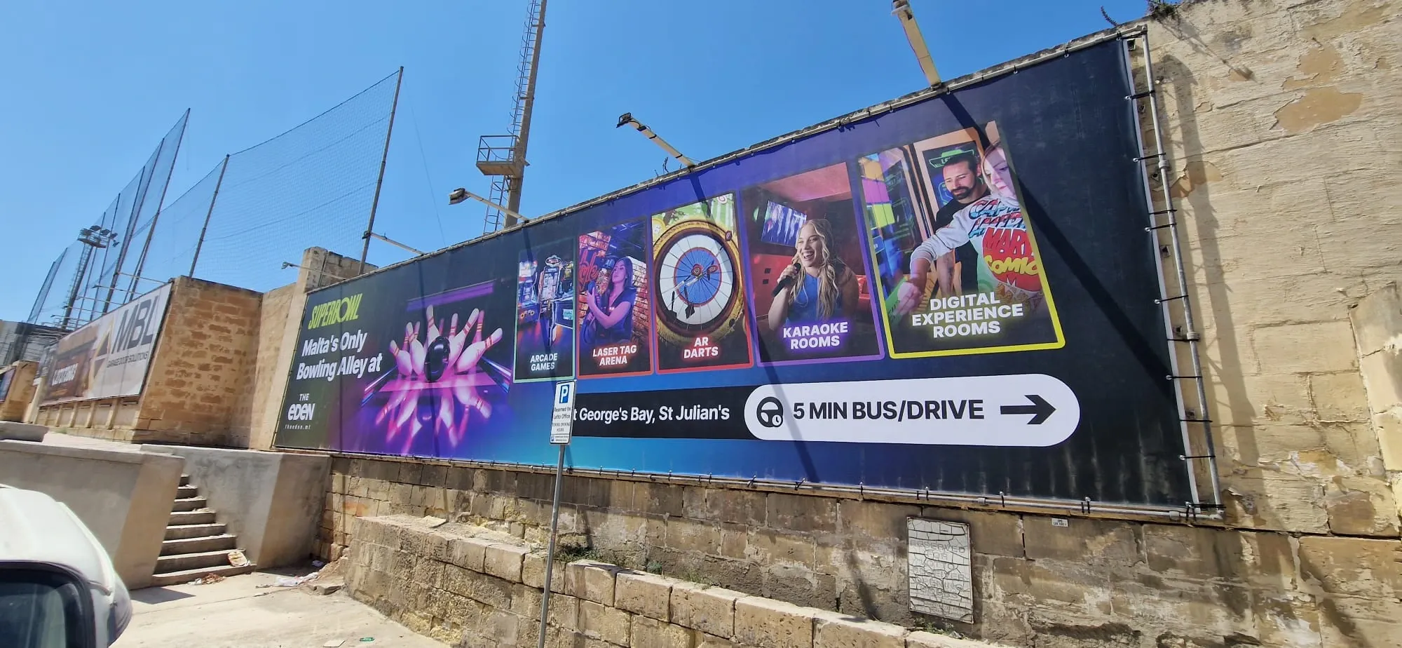 Wide dark banner with photographic panels for bowling, darts and karaoke rooms fixed along a stone site hoarding