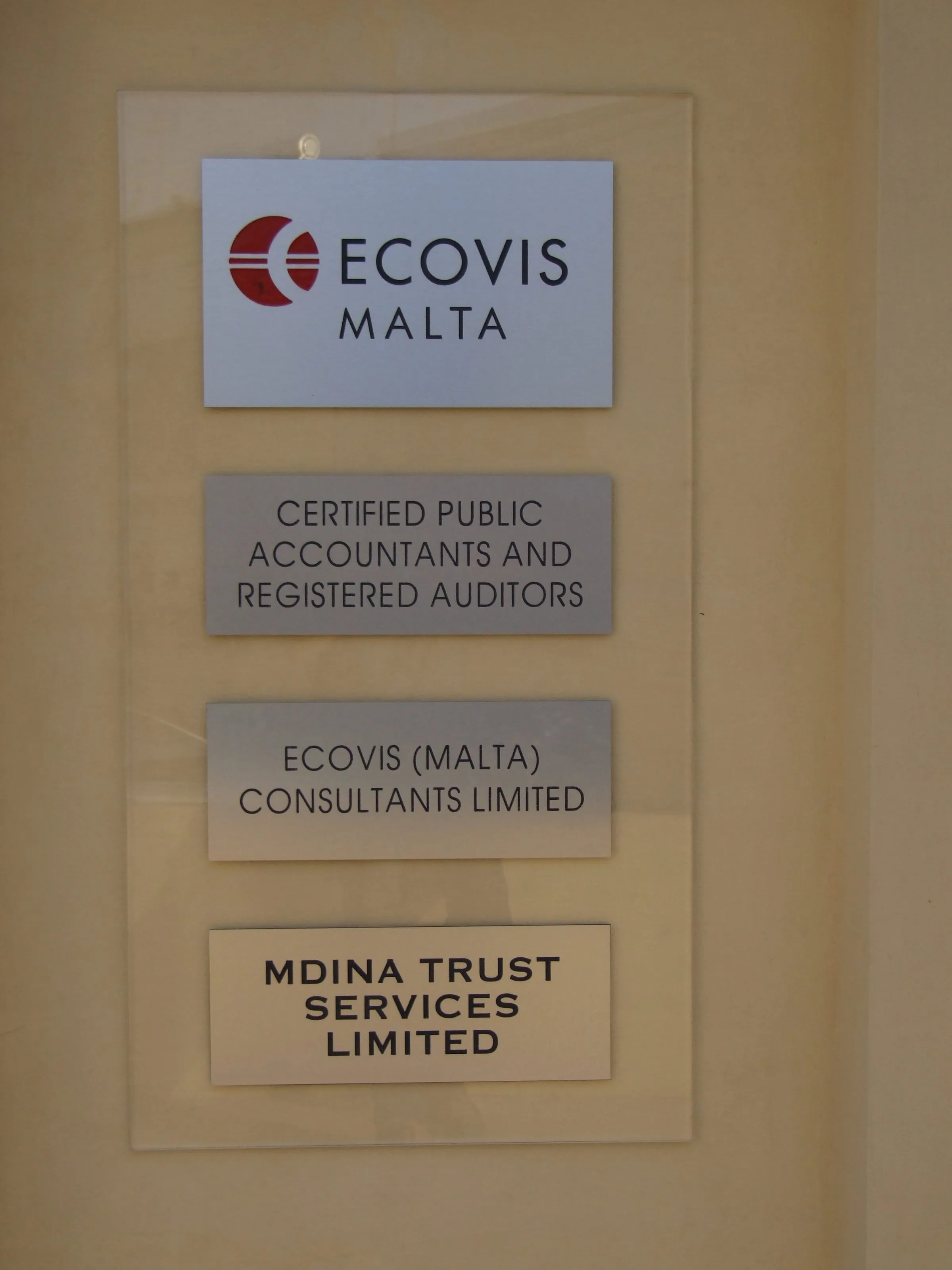Three stacked acrylic plaques on standoff fixings printed with company names, mounted on stone