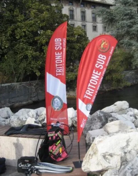 Two red and white printed feather flags on ground spikes beside rocks at an outdoor event