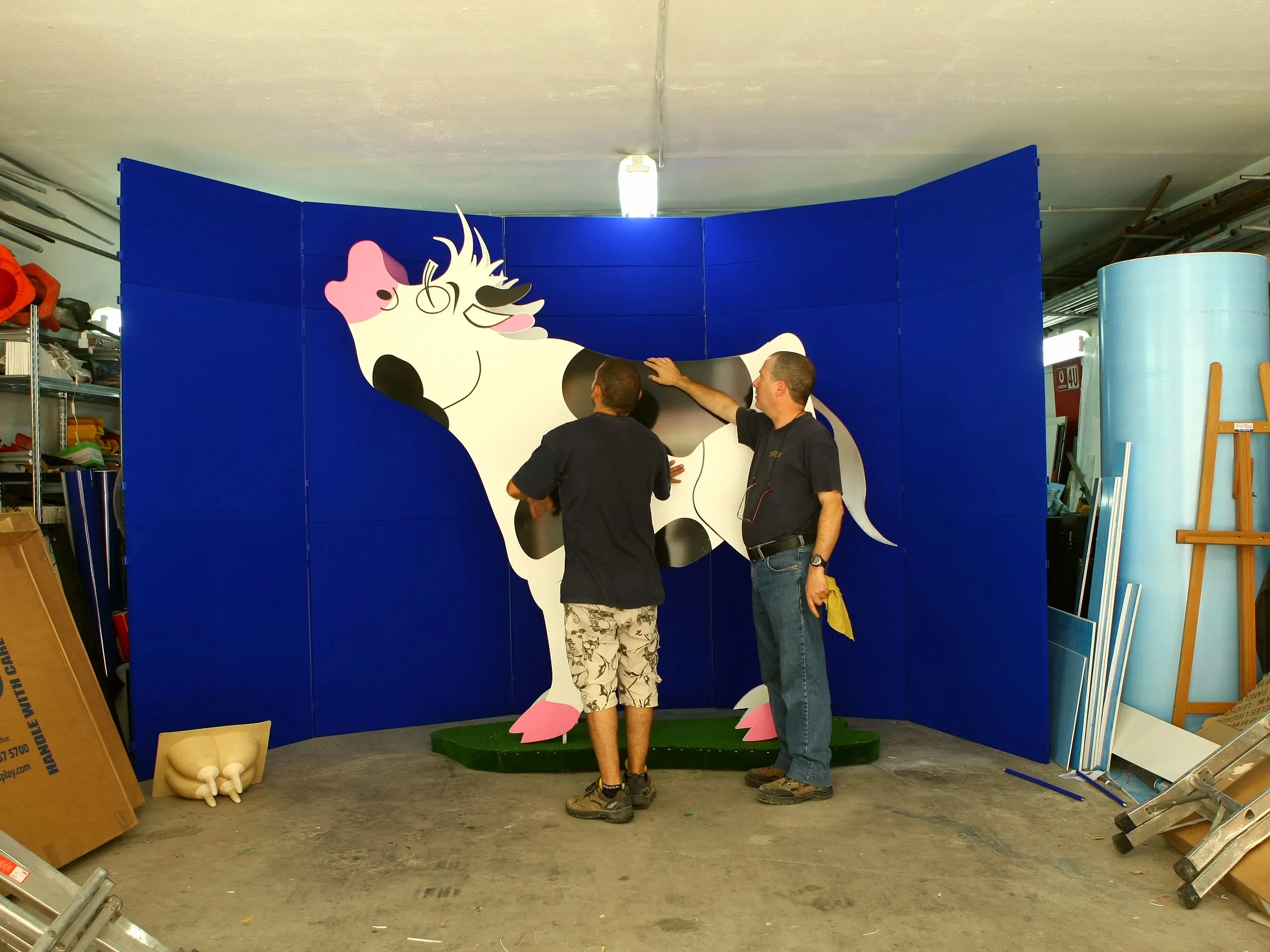 Full-size fabricated cow display figure on a circular base while a worker adjusts the finish