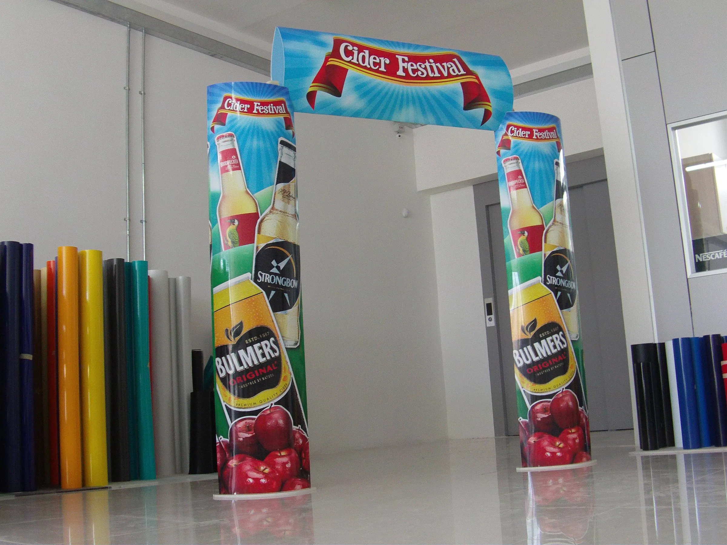 Printed entrance arch with fruit imagery standing in a workshop beside rolls of vinyl