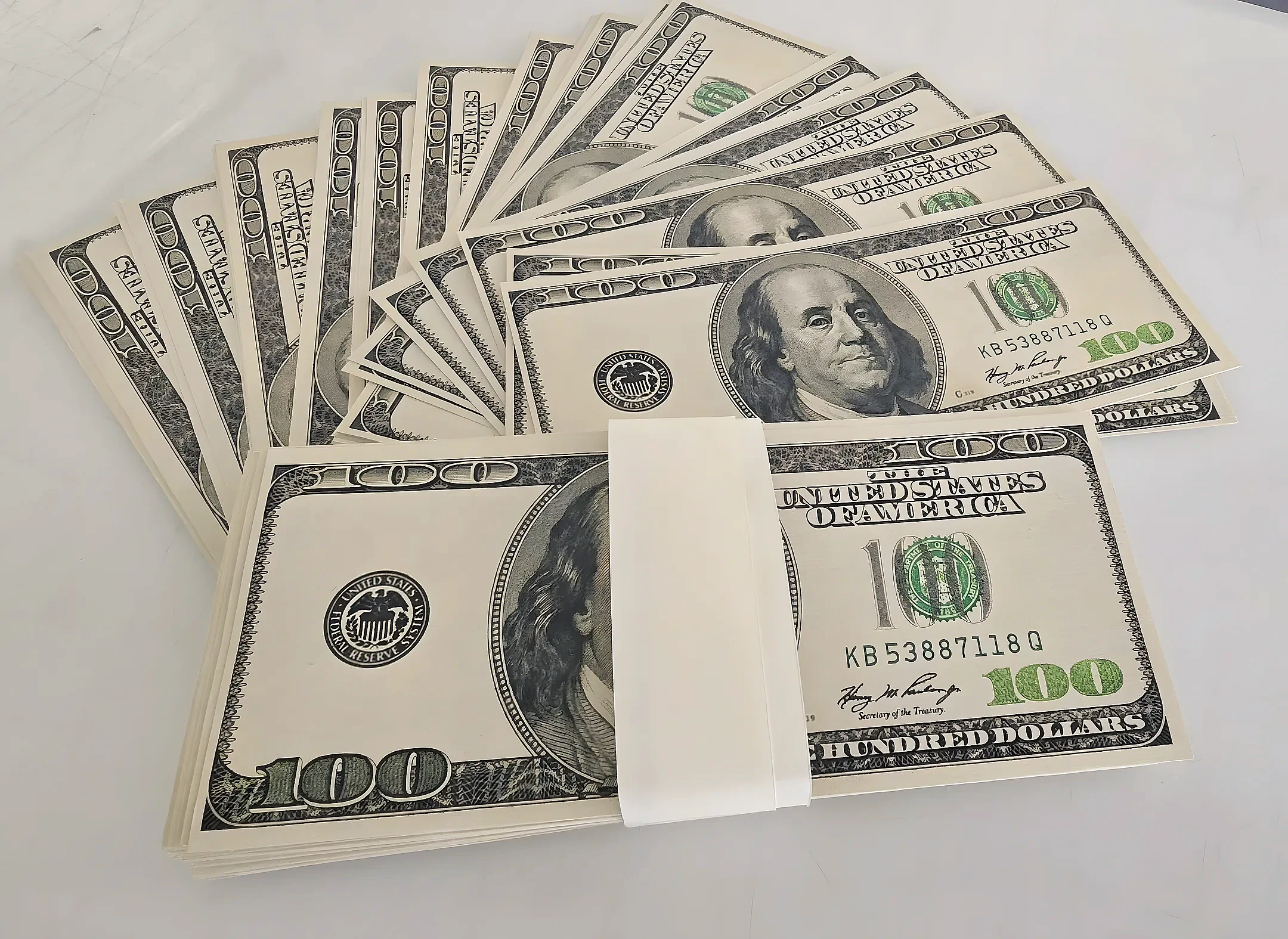 Fanned stacks of printed prop hundred dollar film notes banded together on a white surface