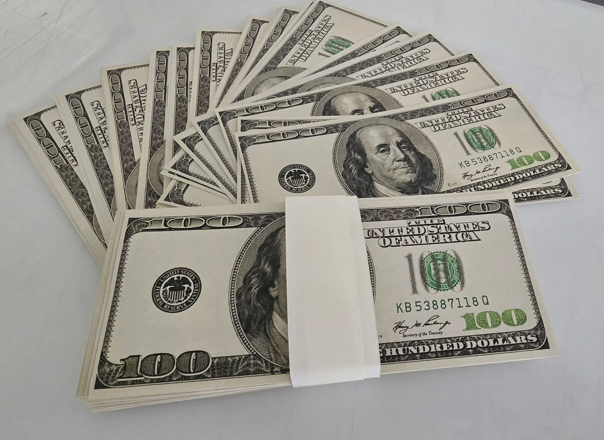 Fanned stacks of printed prop hundred dollar film notes banded together on a white surface