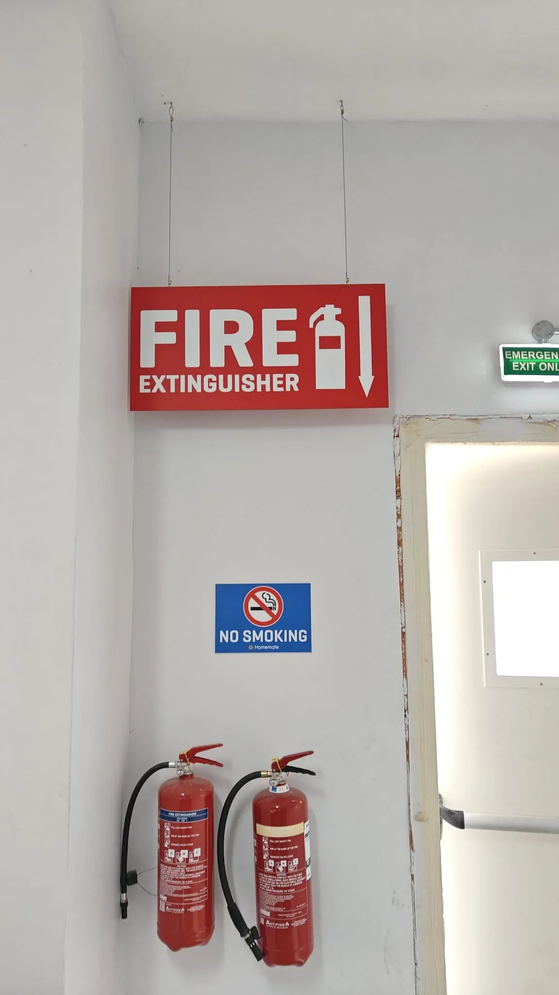 Red fire extinguisher sign suspended above two extinguishers with a no smoking plate below