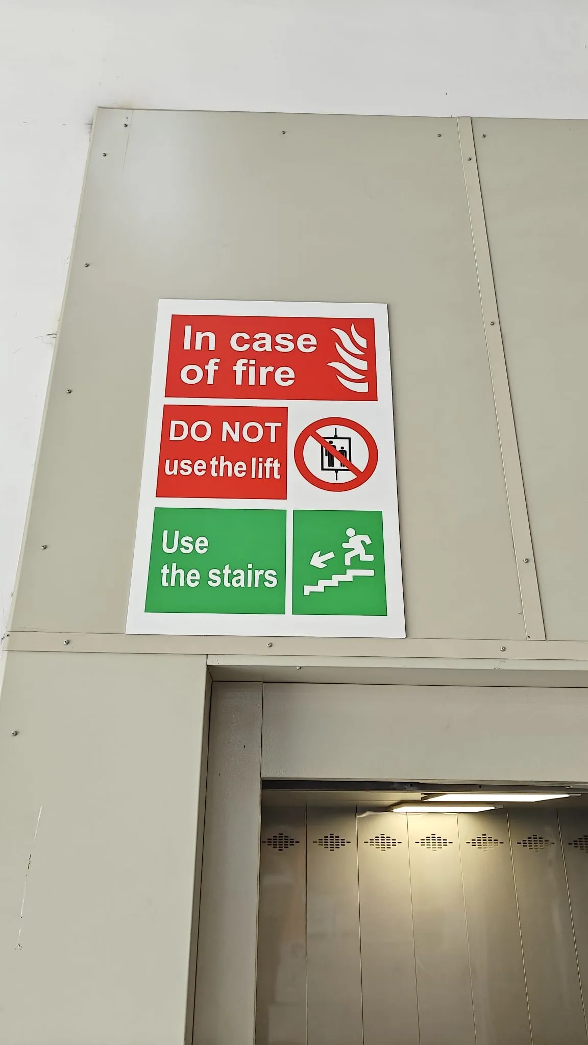 Red and green in case of fire notice fixed above a lift entrance