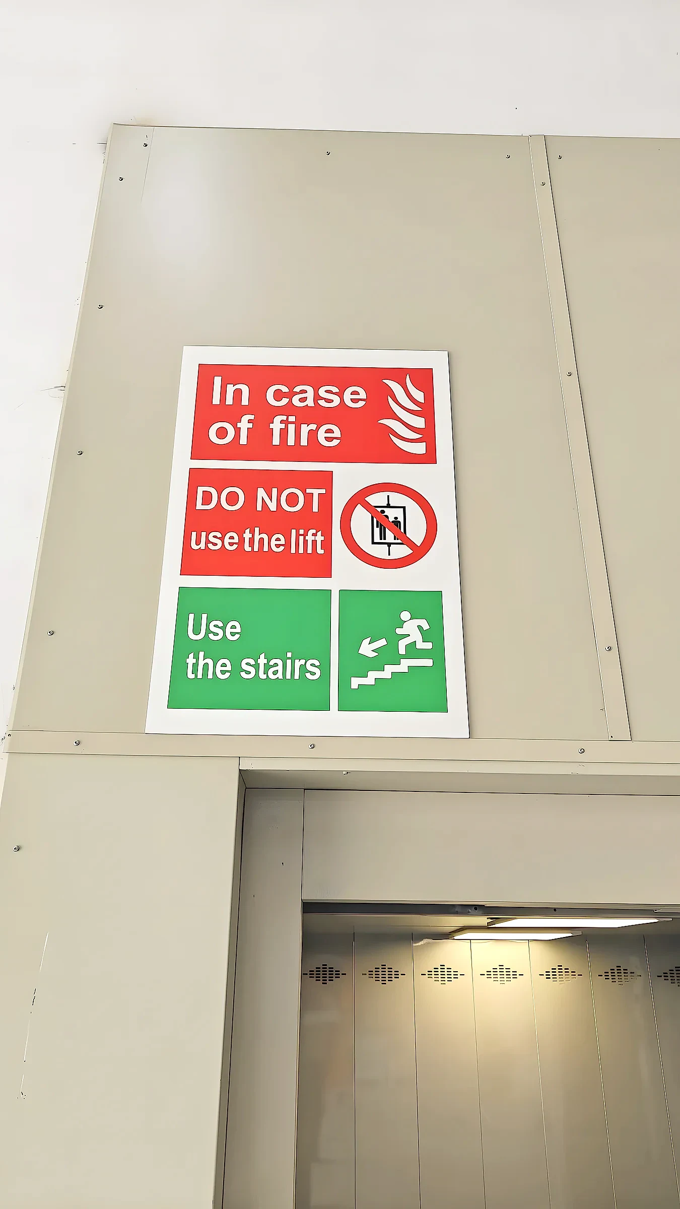 Red and green in case of fire notice fixed above a lift entrance
