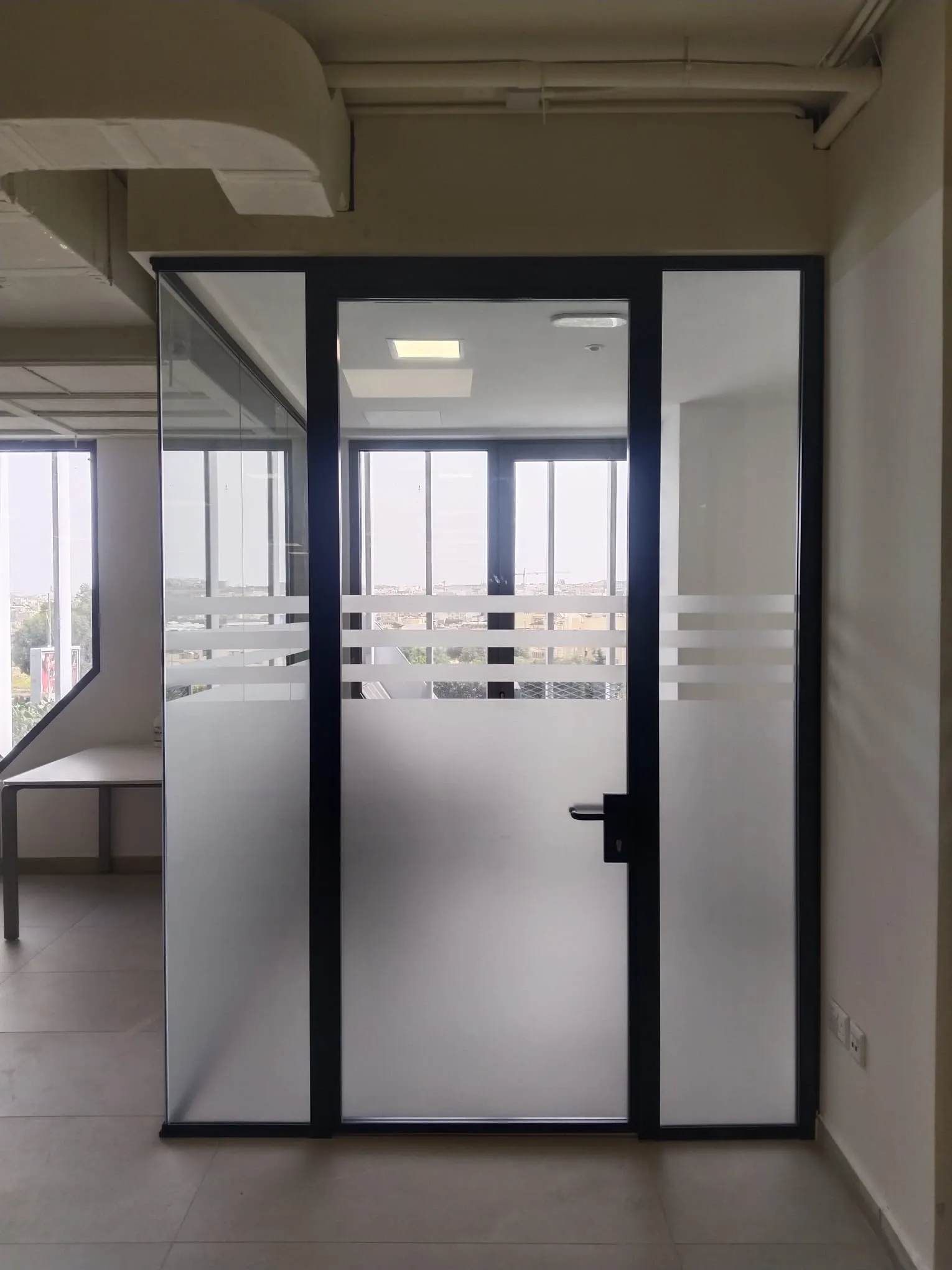 Glass office partition and door with frosted film below and horizontal frosted bands at eye level