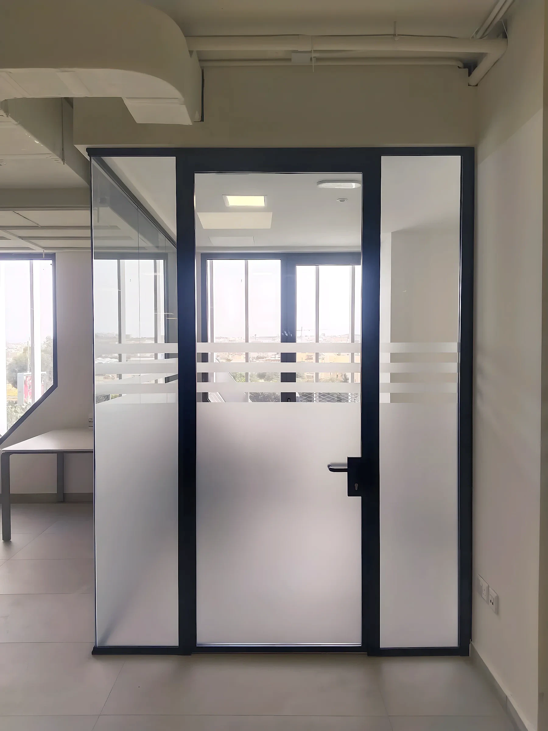 Glass office partition and door with frosted film below and horizontal frosted bands at eye level
