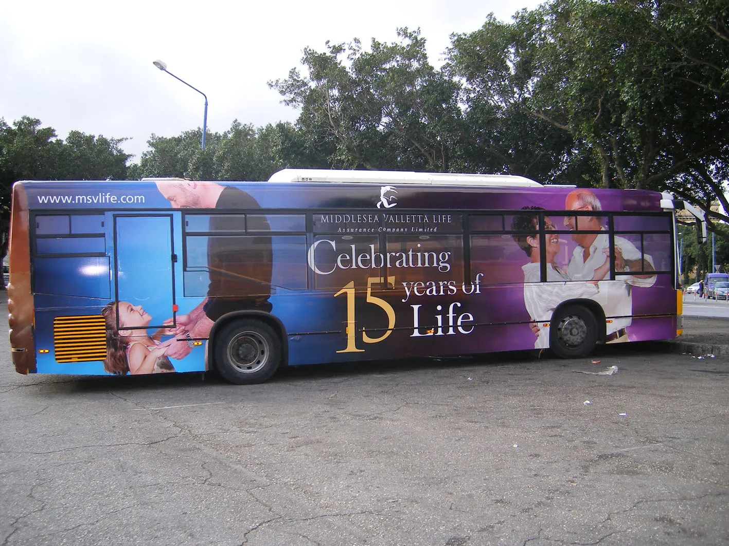 City bus wrapped end to end in photographic portraiture on a purple and blue ground, the print running across the window glazing and around onto the rear