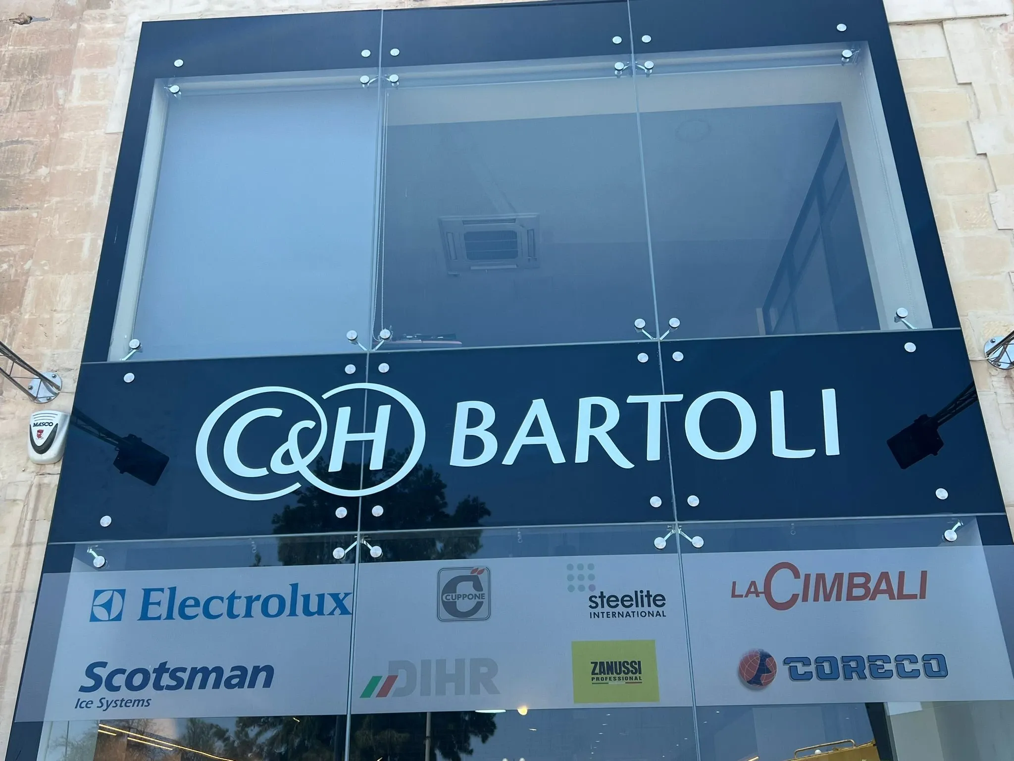 Dark fascia sign with large built-up lettering above a white panel of supplier logos on a glazed frontage